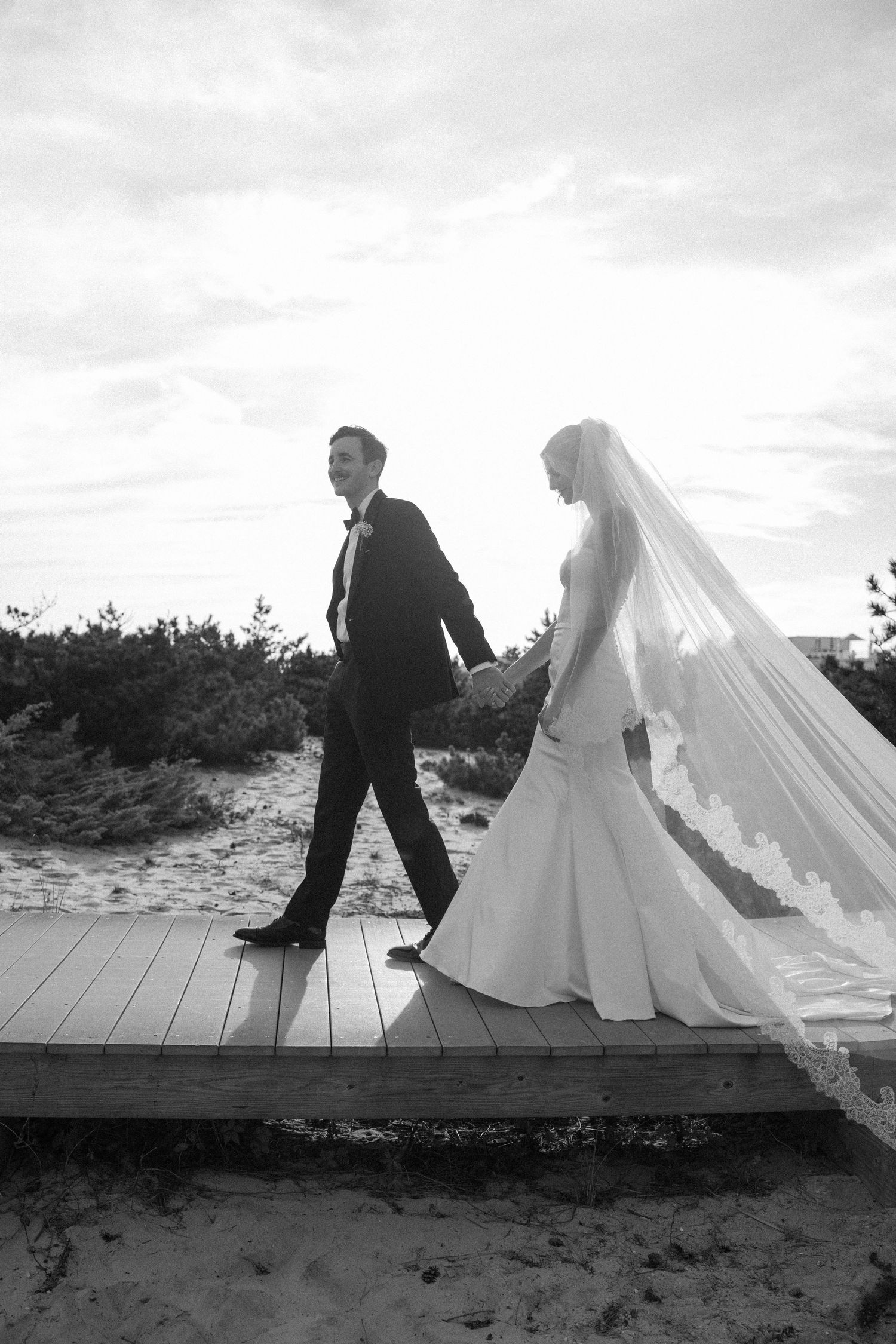 Couple poses on wooden boardwalk at beach with ocean in background.