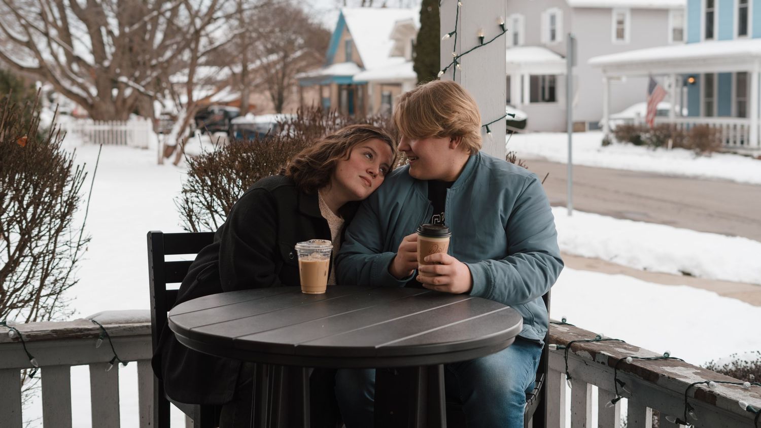 A couple sitting at a table outside, enjoying hot drinks in a snowy setting.