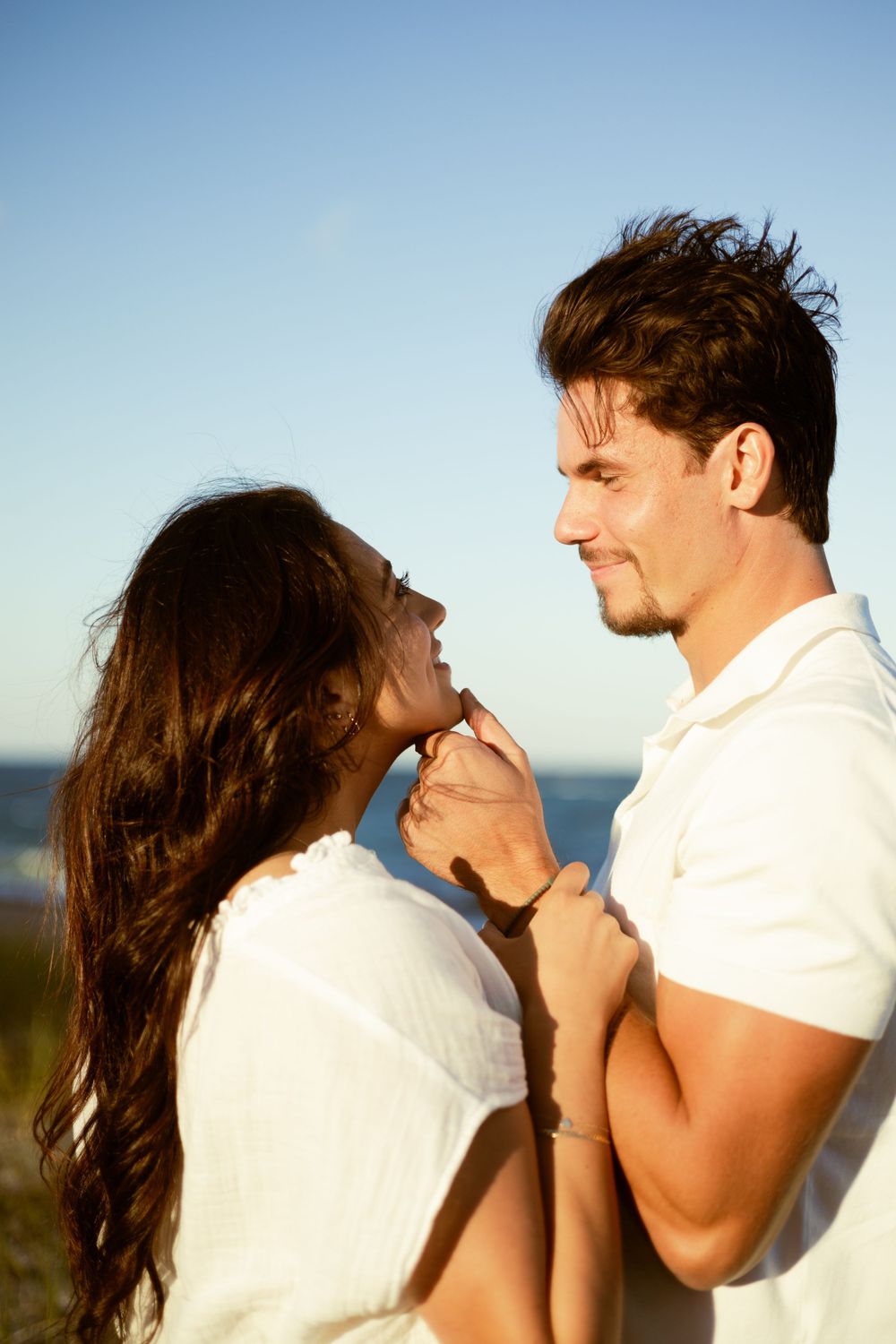a man holding his girlfriend's chin with his thumb and smiling down at each other
