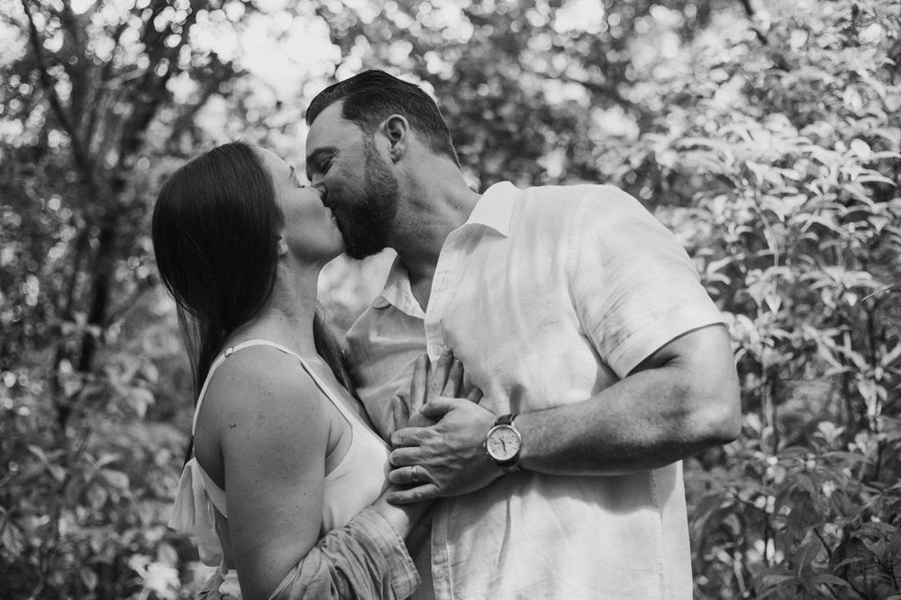 Black and white image of a couple kissing in front of trees.