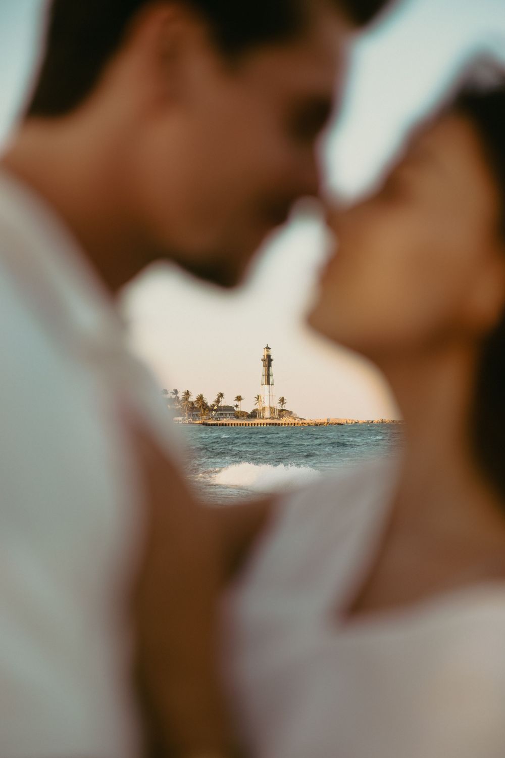 couple touching noses and lighthouse and ocean framed between them