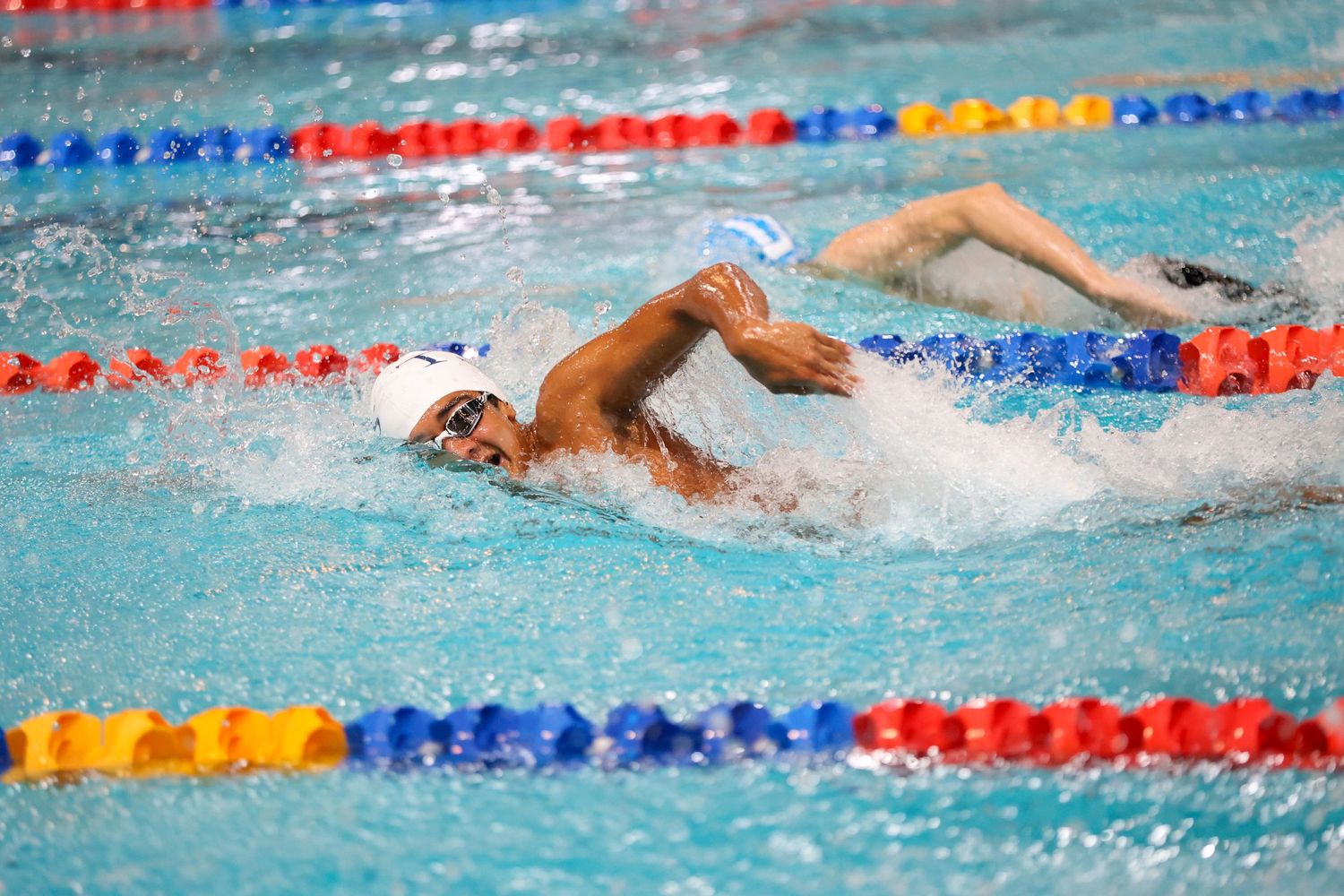Competitive swimmer performing freestyle stroke in a pool with lane dividers.