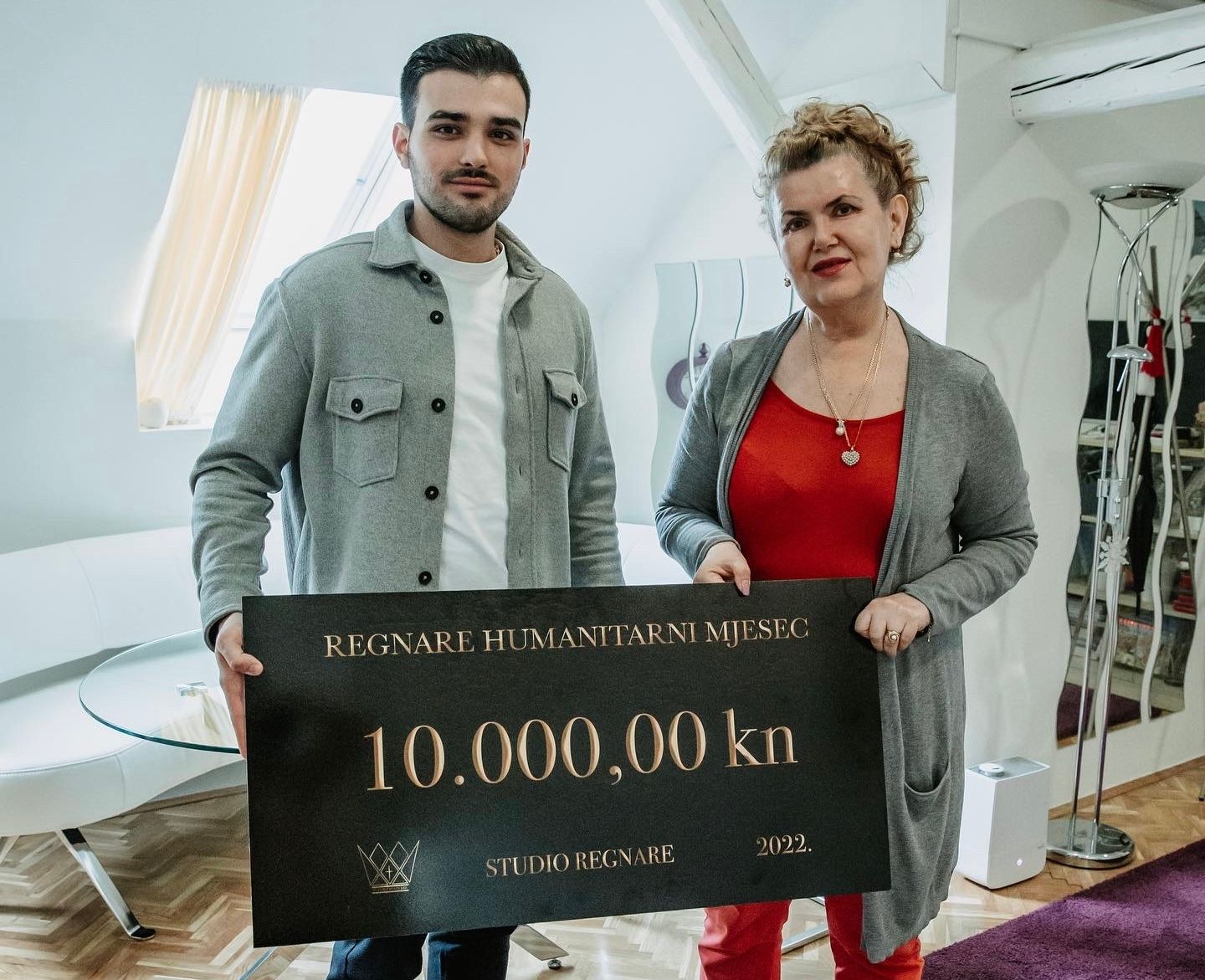 Two people holding a large ceremonial check for 10,000 kn in an indoor setting.