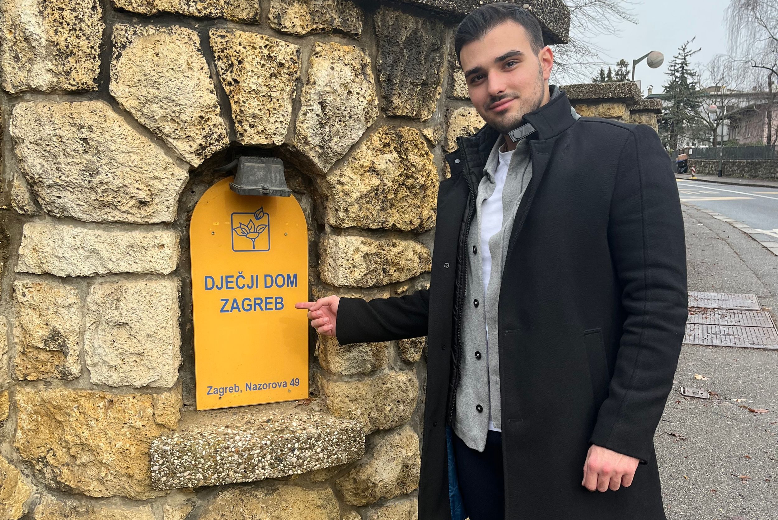 Person standing next to a yellow postbox mounted on a stone wall.