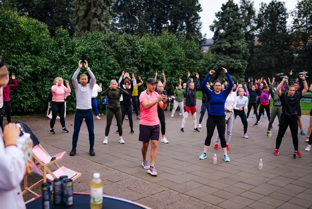 Fitness participants raising arms during synchronized group exercise in a park.