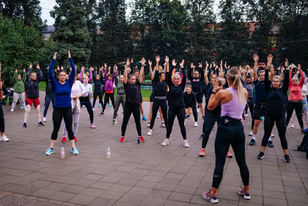 Large group doing synchronized aerobic exercises outdoors with arms raised.