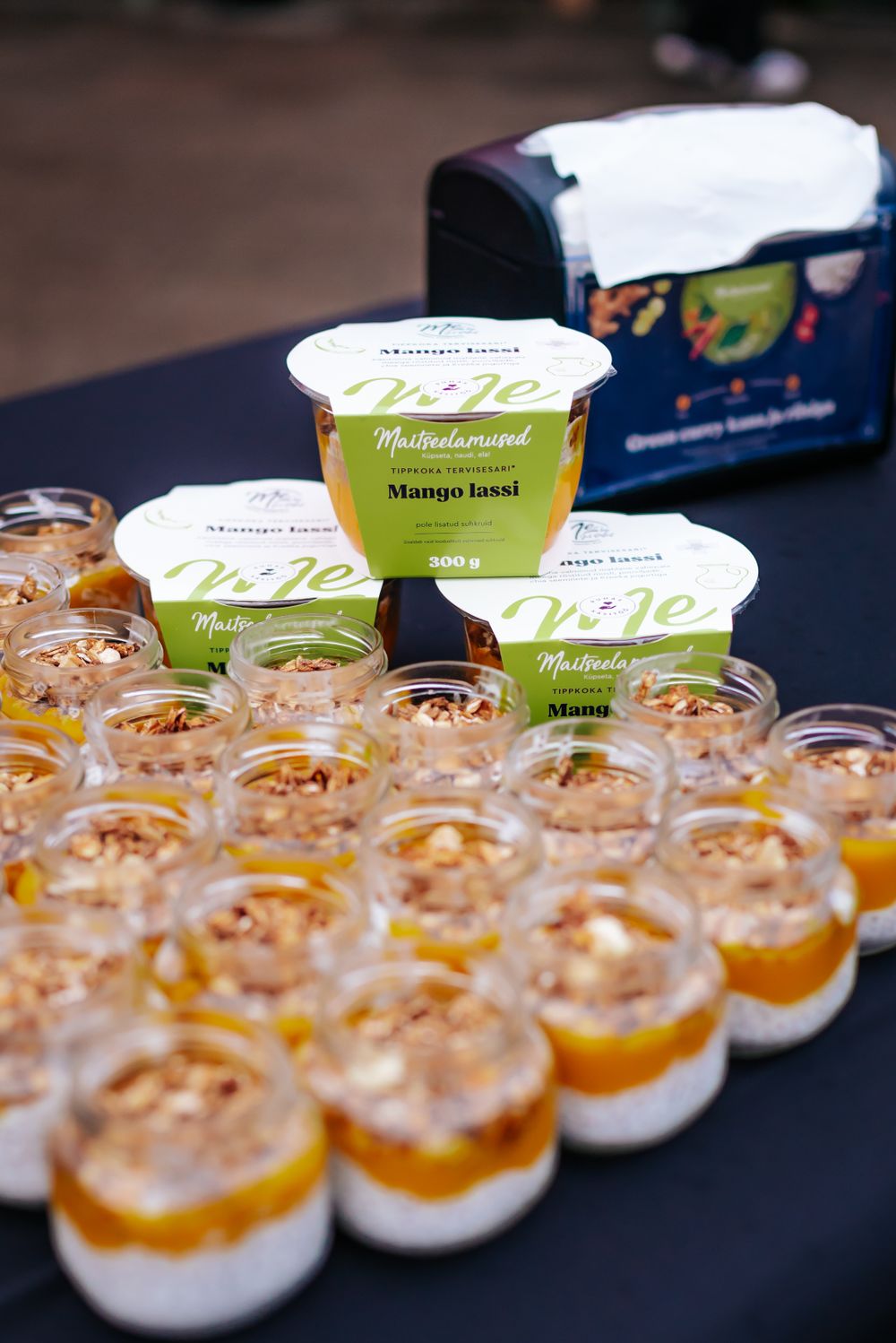 Rows of individual dessert cups arranged on a black table with yogurt containers in background.