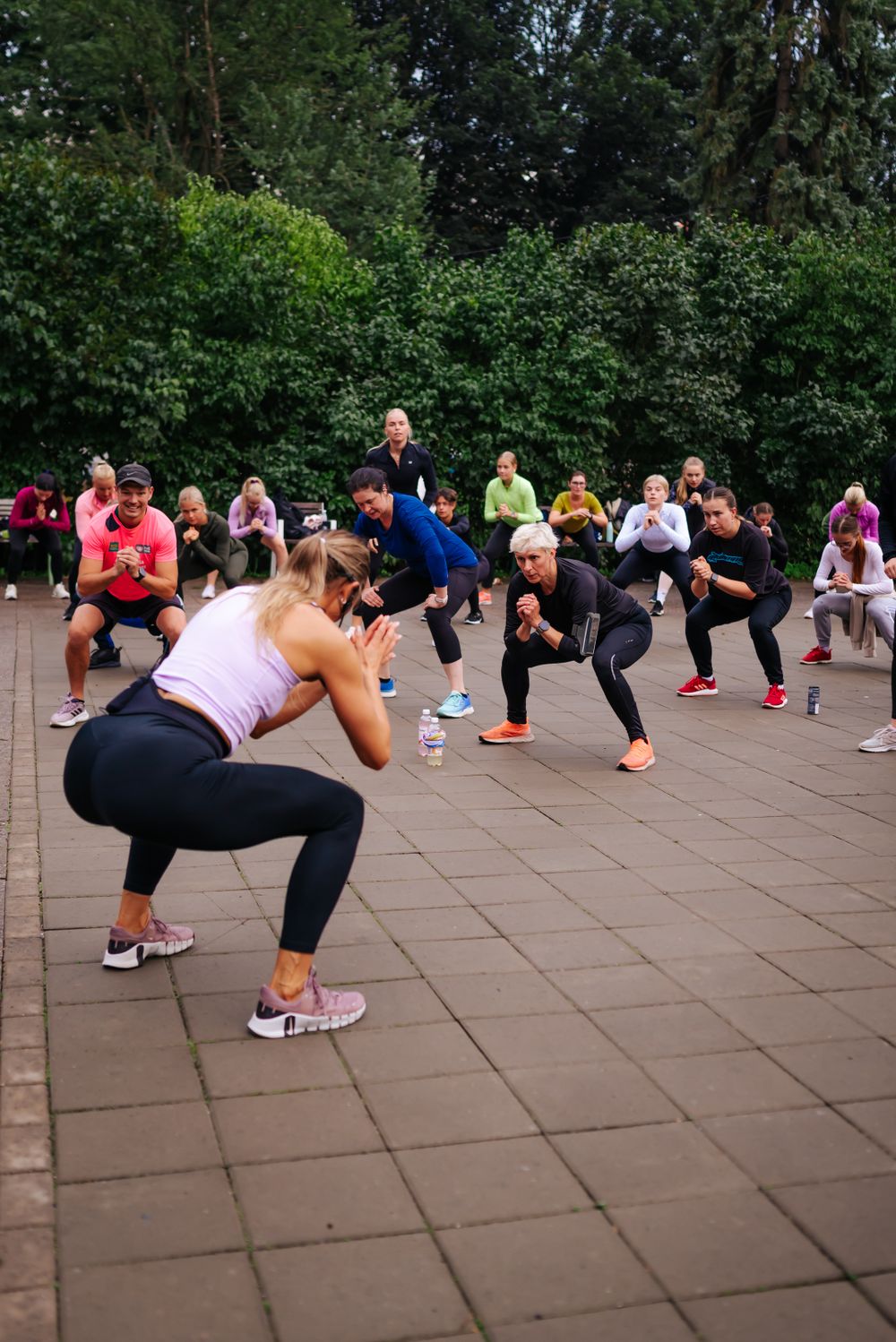 Large group of fitness enthusiasts performing squat exercises during an outdoor workout class.