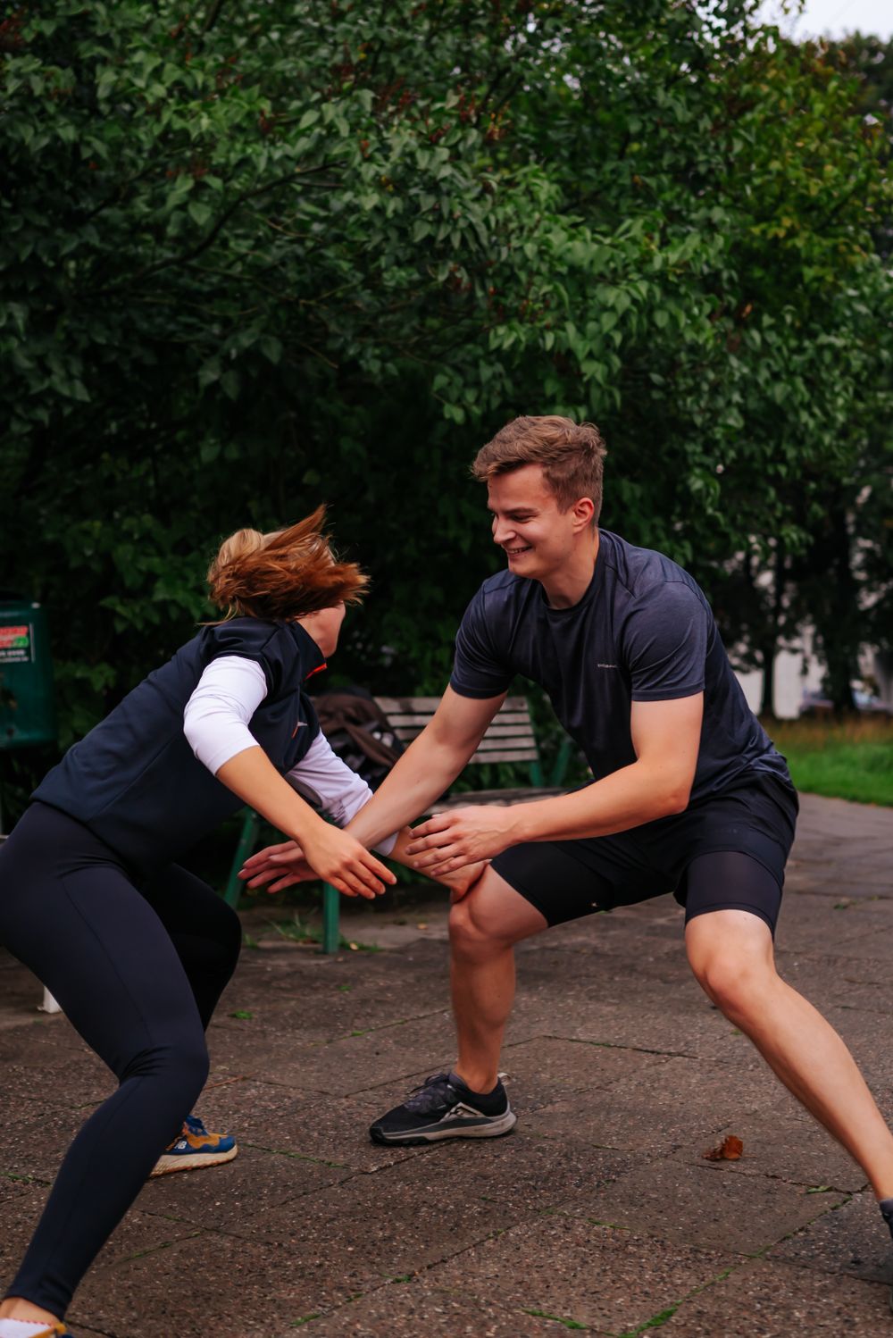 Two people practicing self-defense moves in a park with green foliage background.
