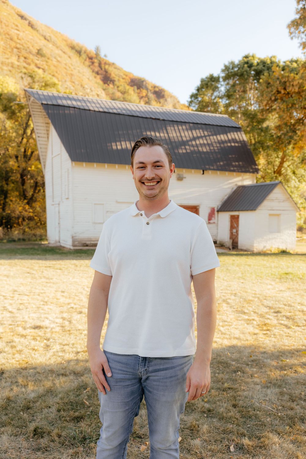 Smiling young man in white polo shirt standing outdoors near a white barn.