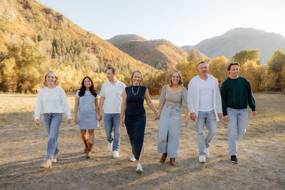 Family of seven walking hand-in-hand through an autumn mountain meadow in coordinated neutral outfits.