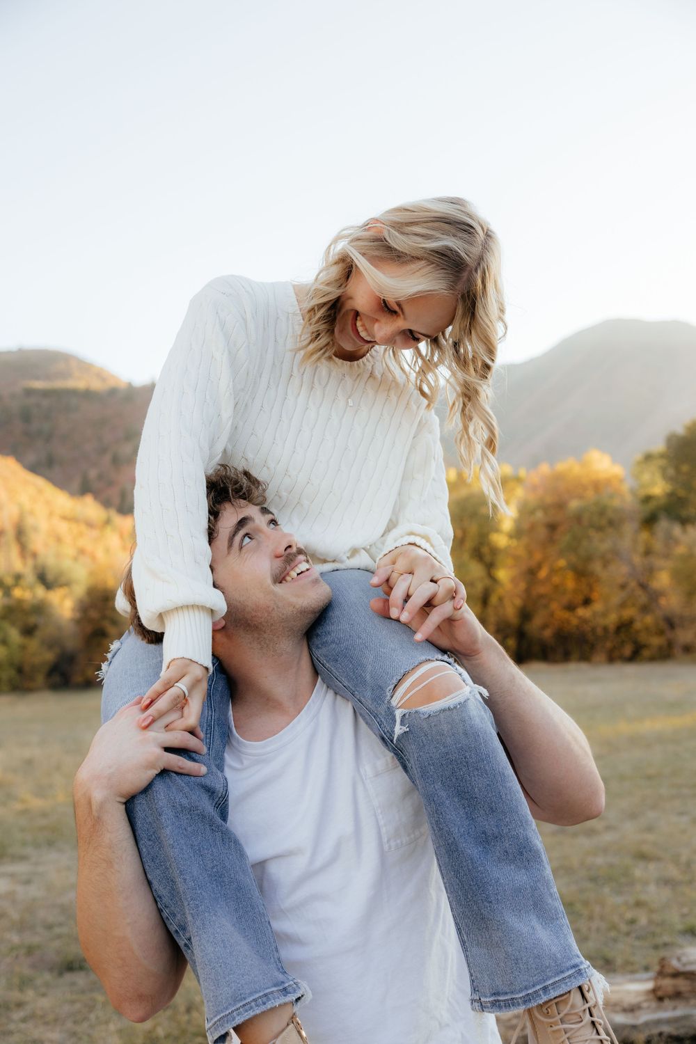 Young man carrying blonde woman on his shoulders in a sunny fall mountain meadow.