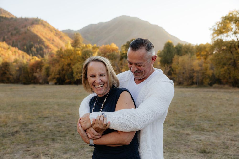 Laughing couple embracing outdoors in a golden autumn mountain field at sunset.