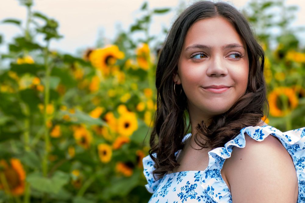Portrait in sunflower garden wearing blue and white ruffled dress.