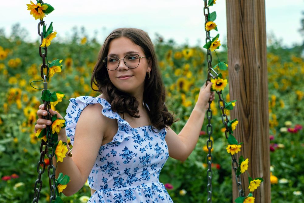 Portrait by wooden post in sunflower field wearing blue floral dress.