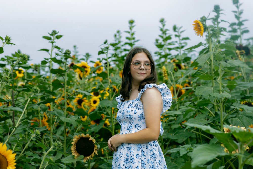 A dreamy garden photoshoot featuring a blue and white floral dress among towering sunflowers.