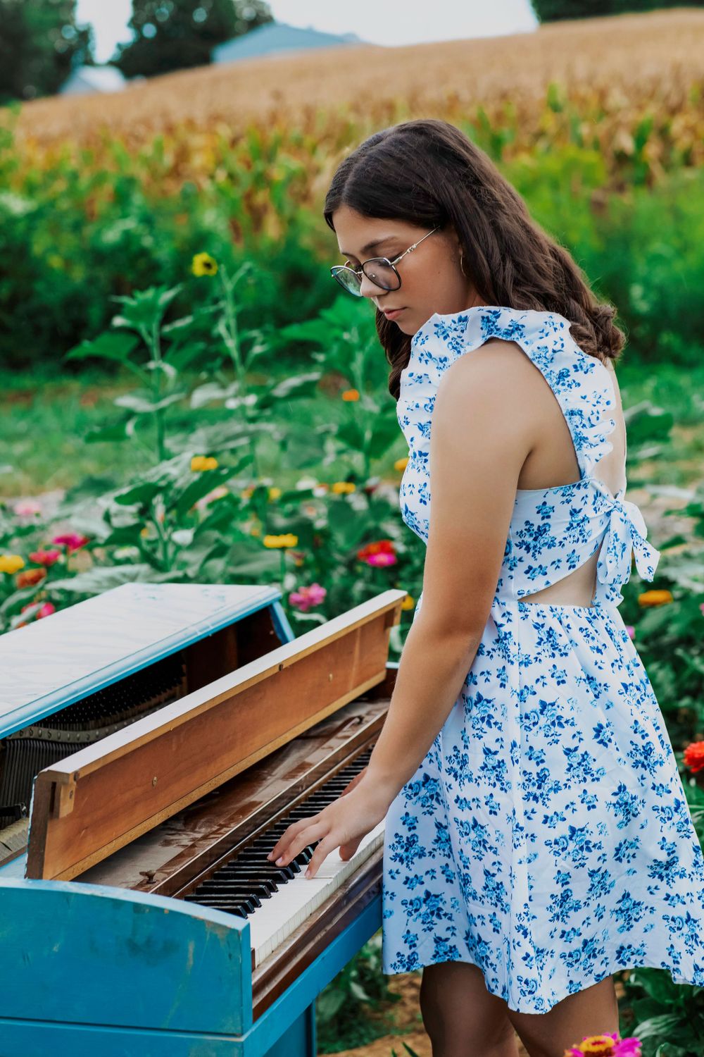 Playing a blue piano outdoors in a flower garden wearing a floral summer dress.