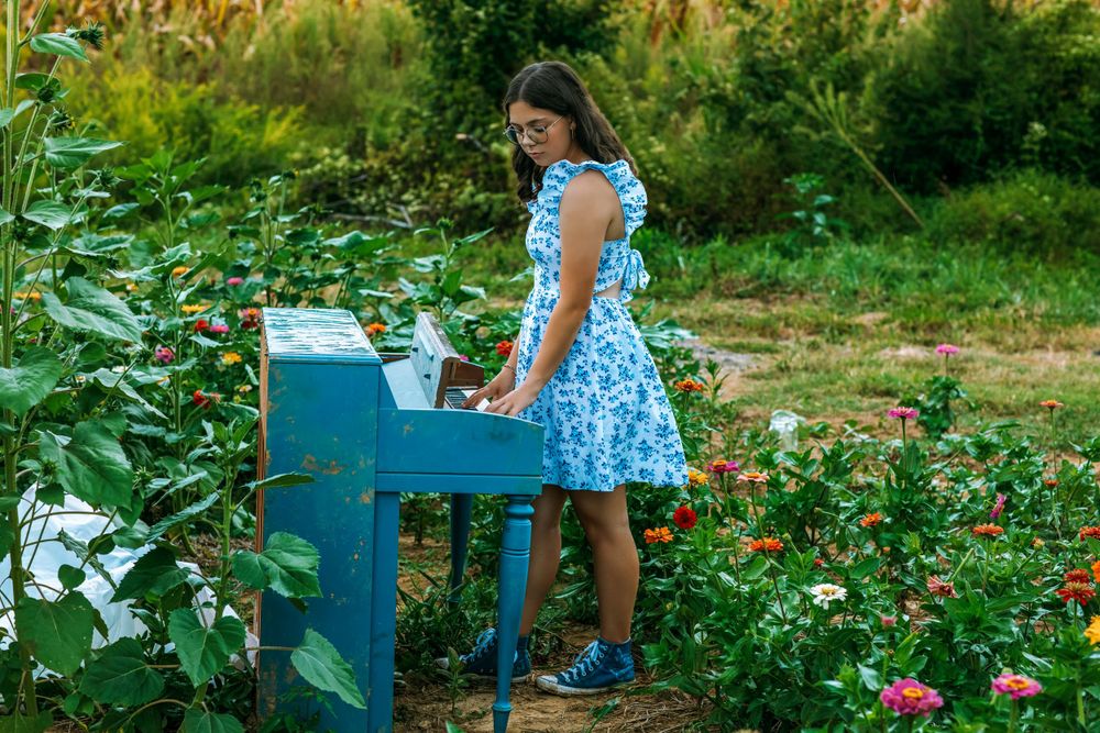 Playing a bright blue piano in a garden setting surrounded by summer flowers.