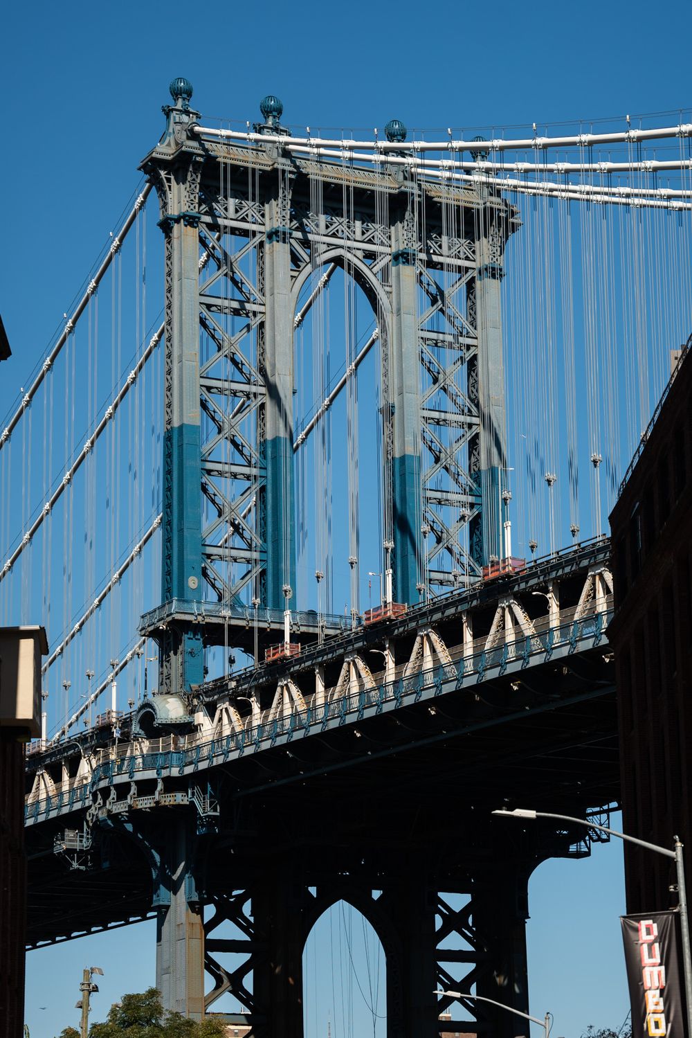 Manhattan Bridge steel towers and cables photographed against bright blue sky.