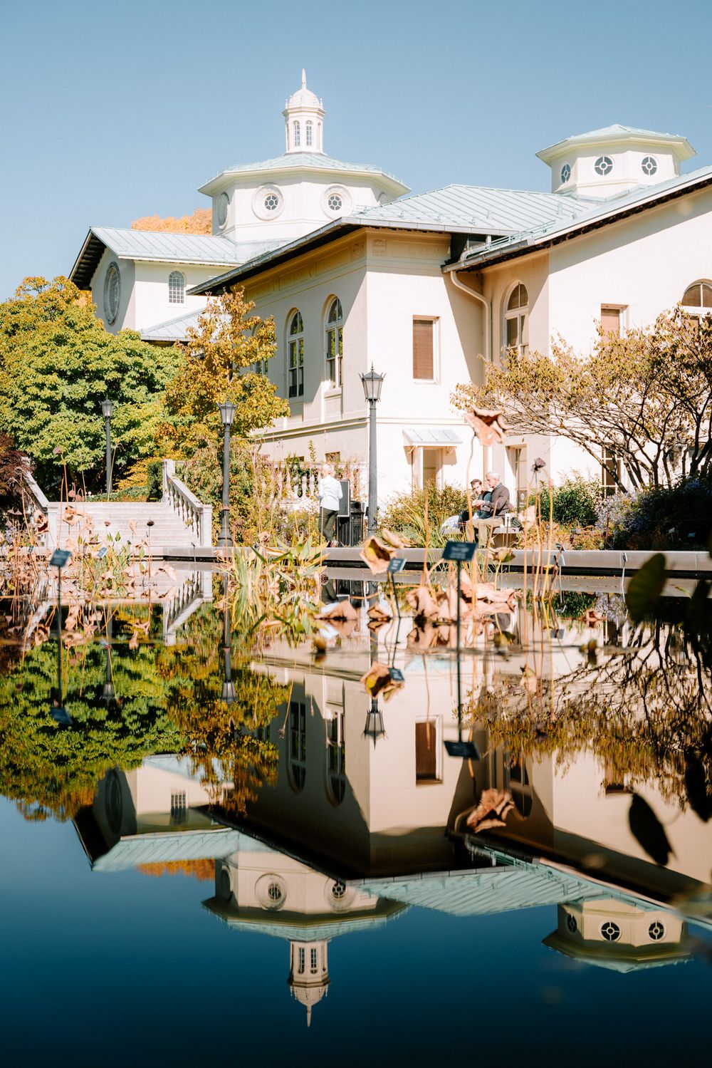 White Mediterranean-style building with domed towers reflecting in still pond surrounded by gardens.