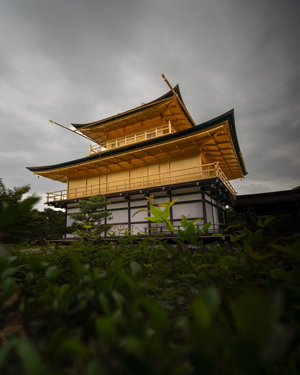 Golden pavilion of Kinkaku-ji temple in Kyoto against dramatic cloudy sky.