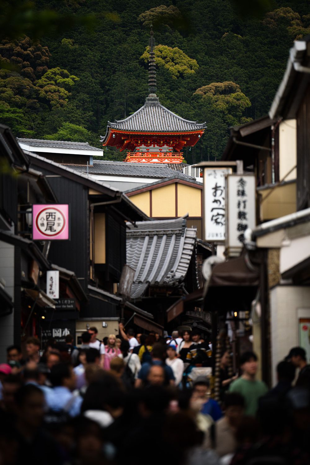 Busy historic street in Kyoto with traditional buildings and red temple visible in background.