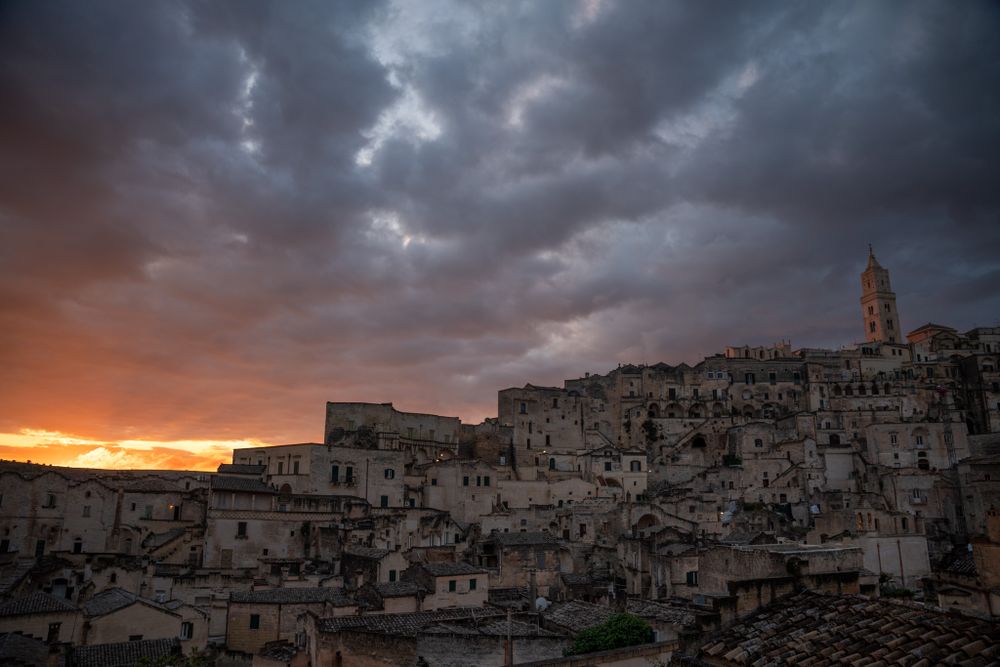 Dramatic sunset over ancient stone buildings in Matera Italy with dark storm clouds gathering above.