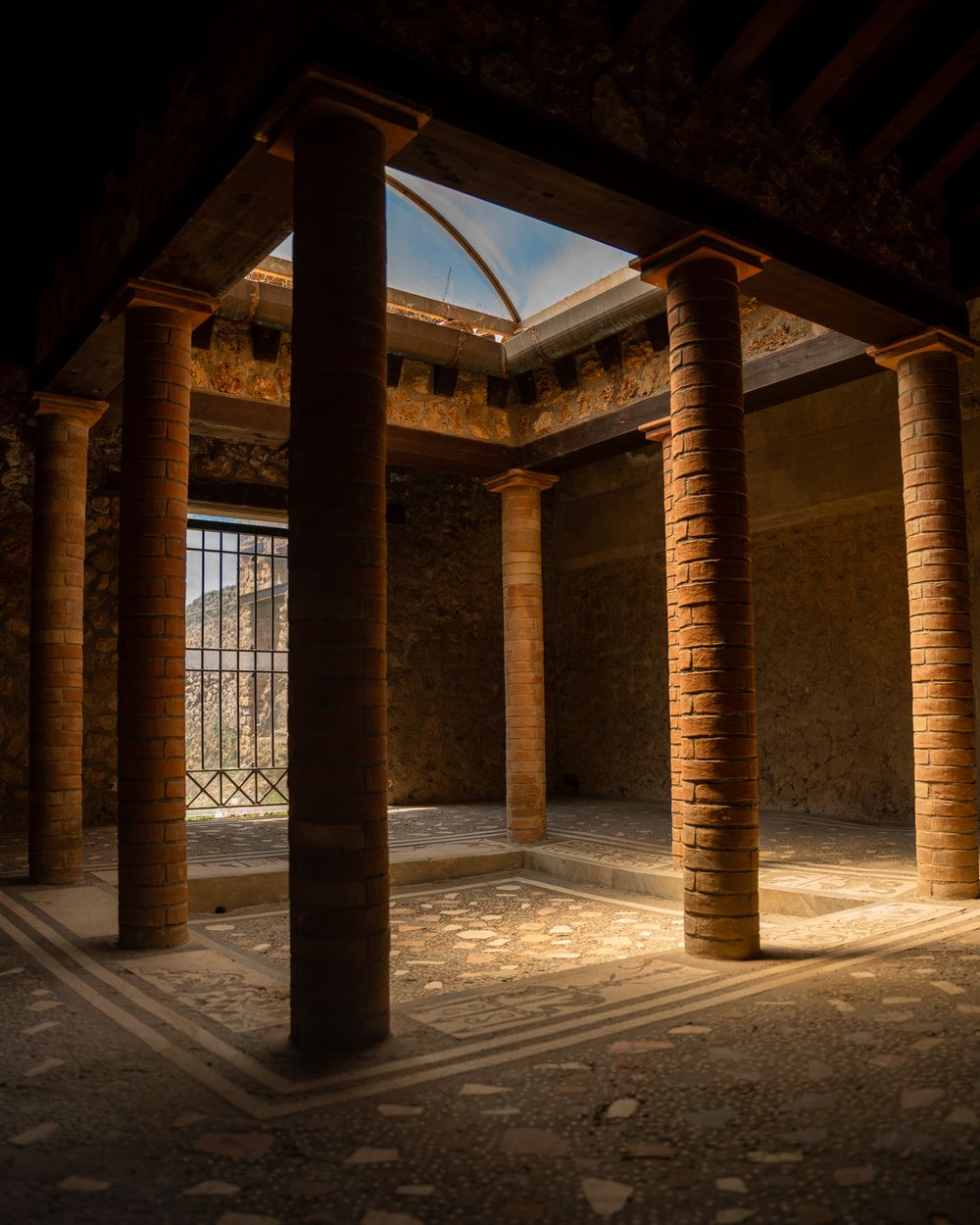 Ancient Roman atrium with stone columns and sunlight streaming through an open roof in Pompeii ruins.