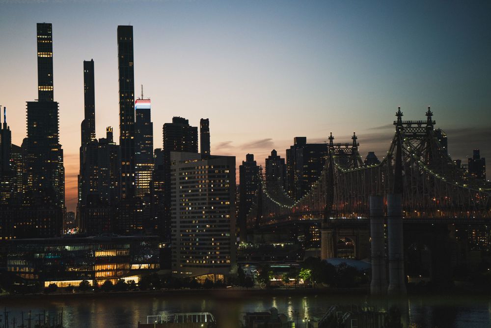 New York City skyline at dusk with illuminated skyscrapers and the Queensboro Bridge.