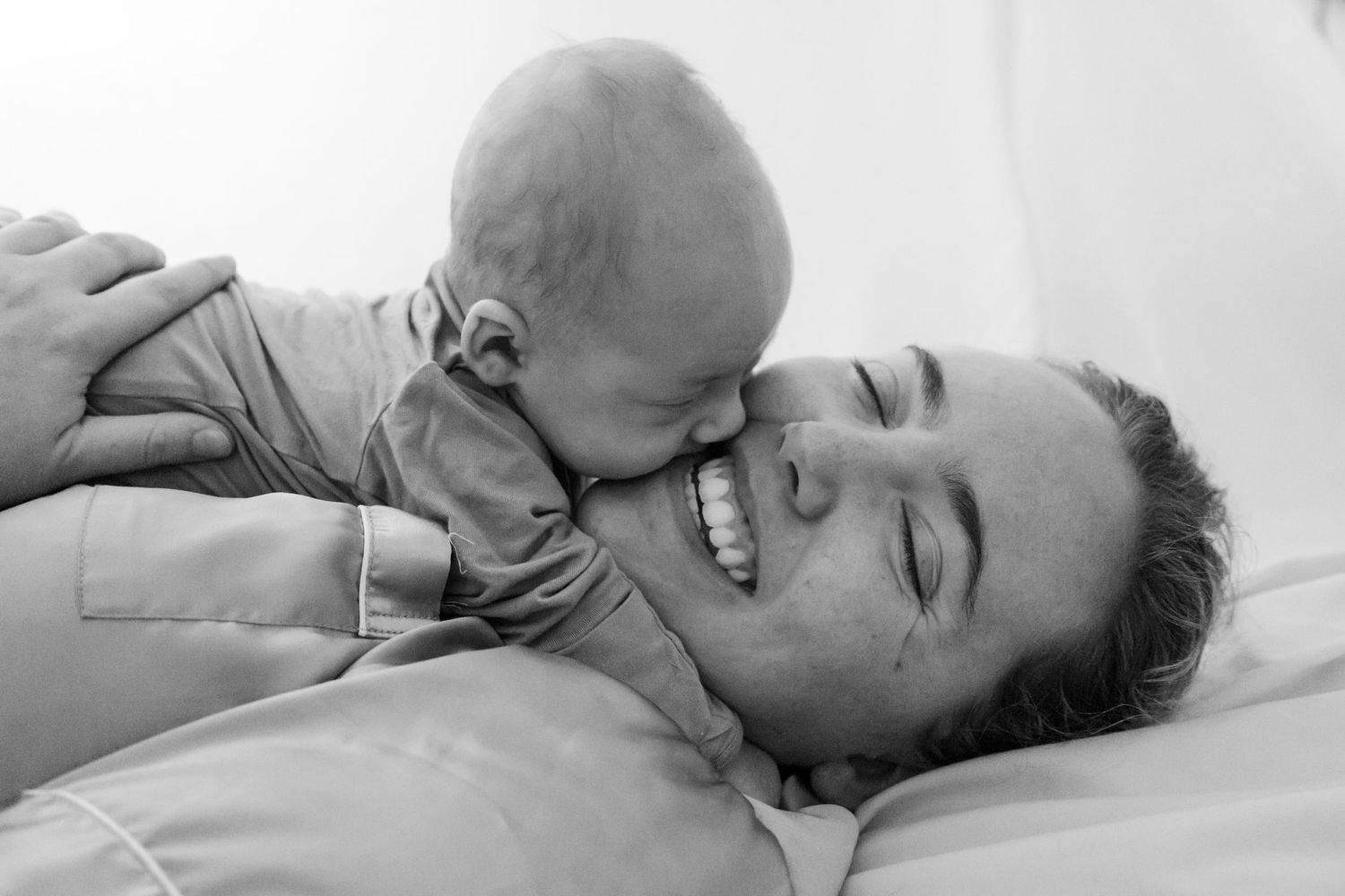 A tender black and white moment shared between parent and baby lying together on soft bedding.