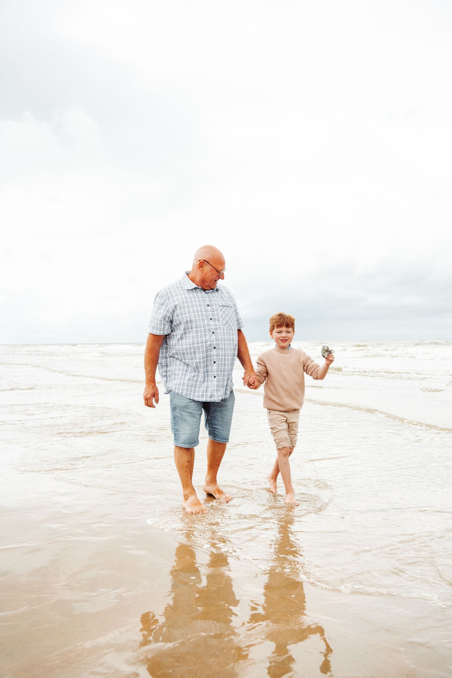 A pair walking barefoot together along the beach shoreline with waves splashing at their feet.