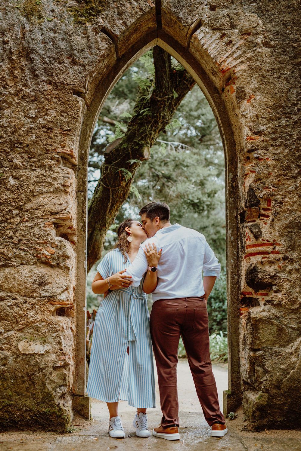 A couple shares a romantic moment under stone archways in a historic setting.