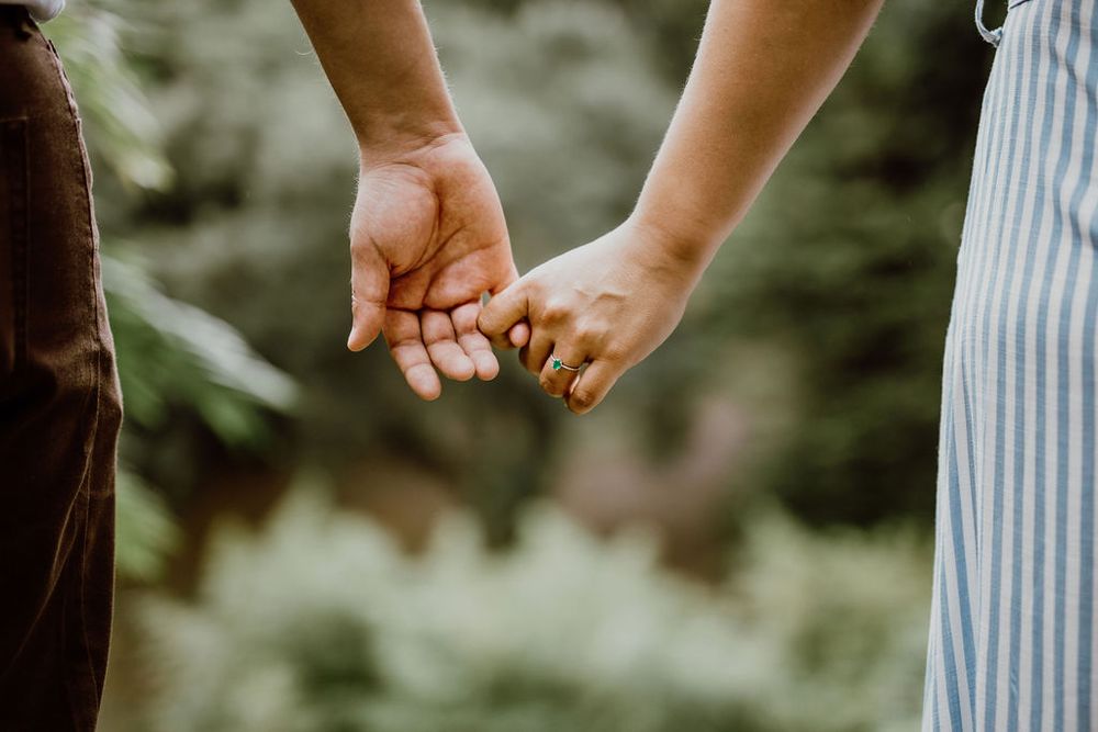 Close-up view of hands holding a delicate white dandelion seed head against a soft blurred green background.