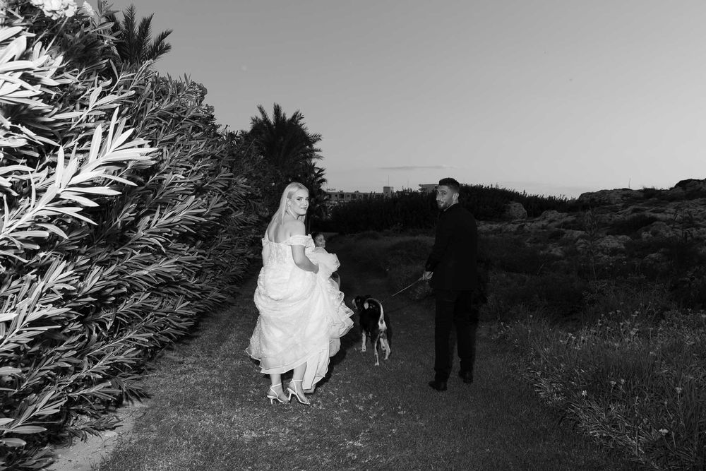 A black and white wedding photo series shows silhouettes of a couple walking through an outdoor path in nature.