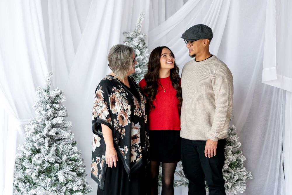 Three family members sharing a warm moment together in a festive winter photo studio setting.