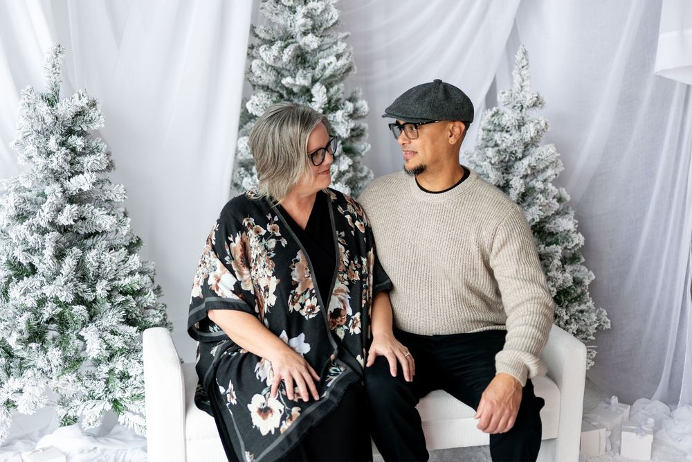 Couple shares a loving glance while seated together in a white winter holiday photo setting.