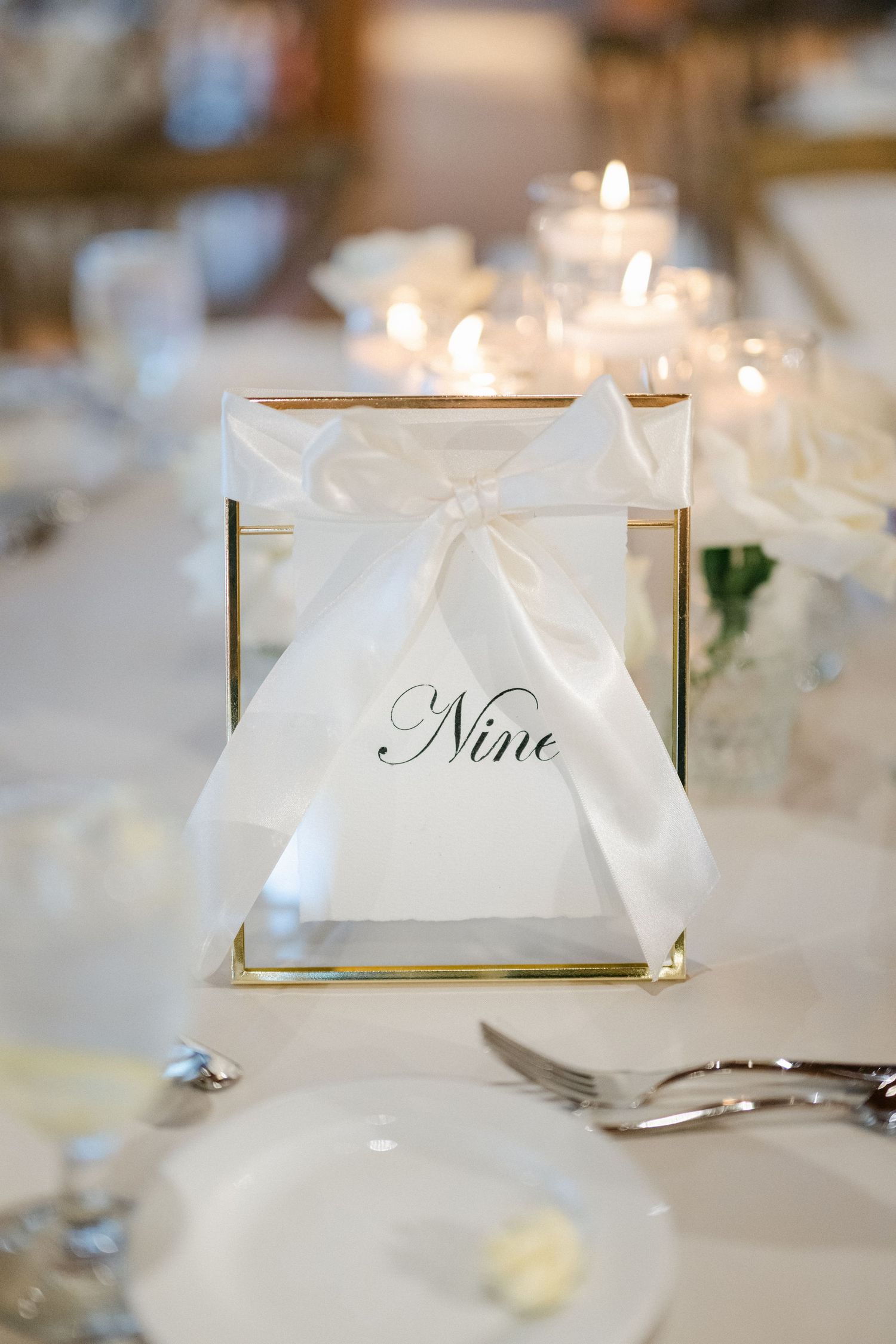 Elegant wedding reception tables set with white linens, crystal glasses and soft candlelight in a rustic wooden venue.