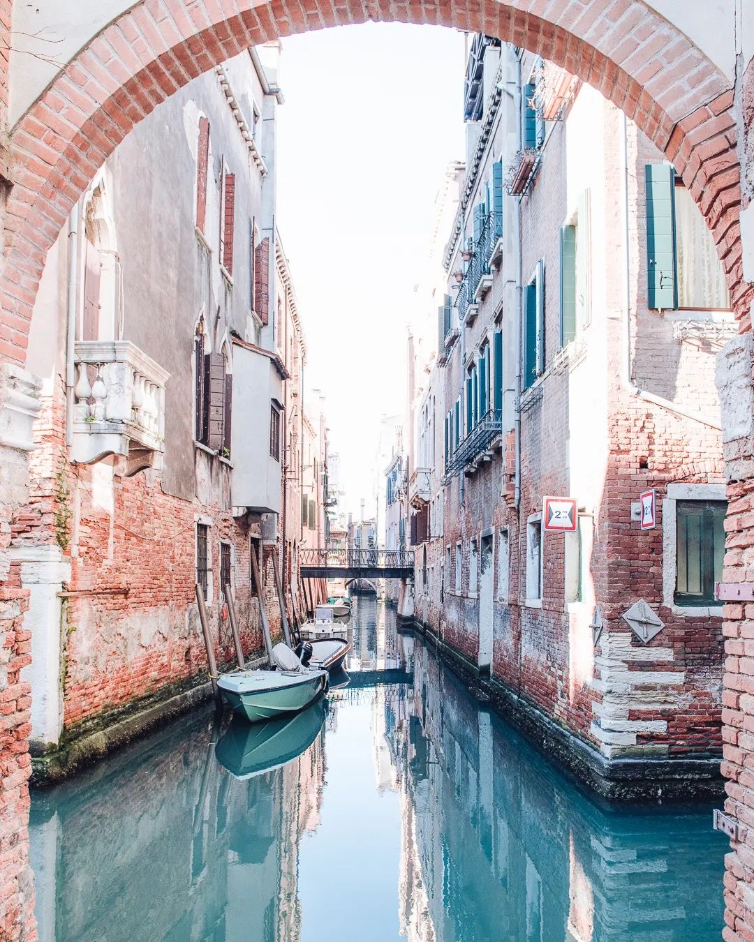 Venice canal seen through a stone archway with historic buildings on both sides.