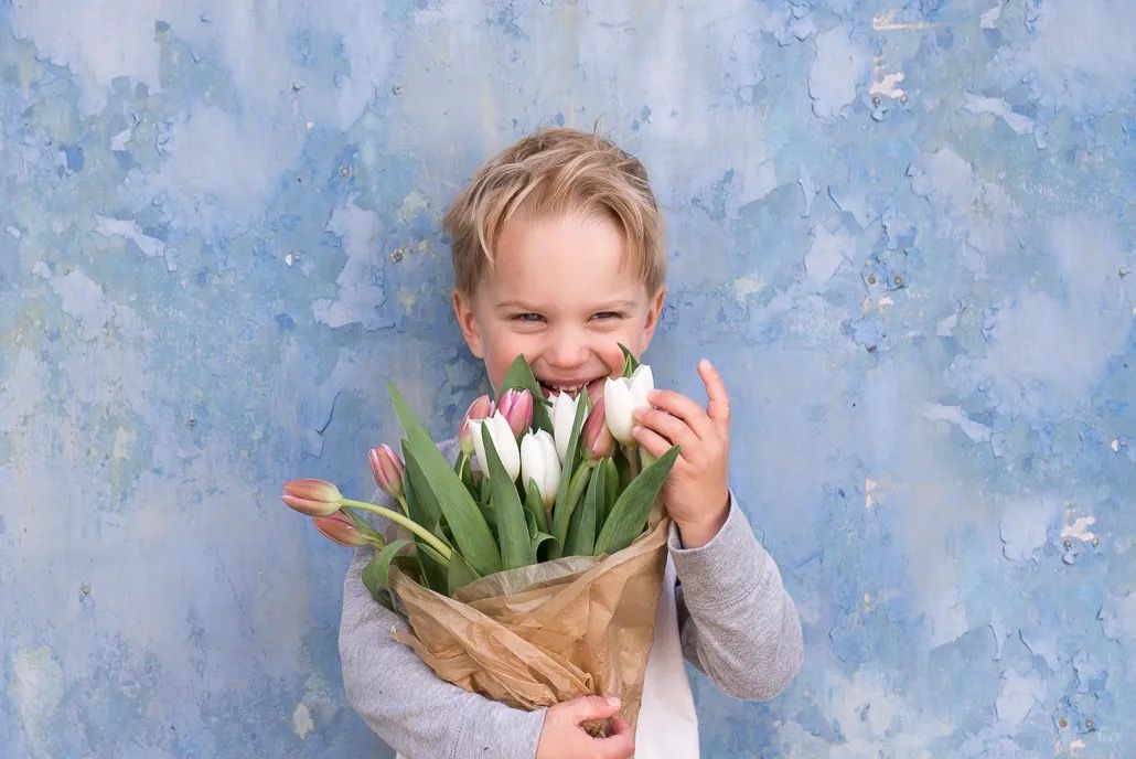 Smiling child holding a bouquet of tulips against a textured blue wall.