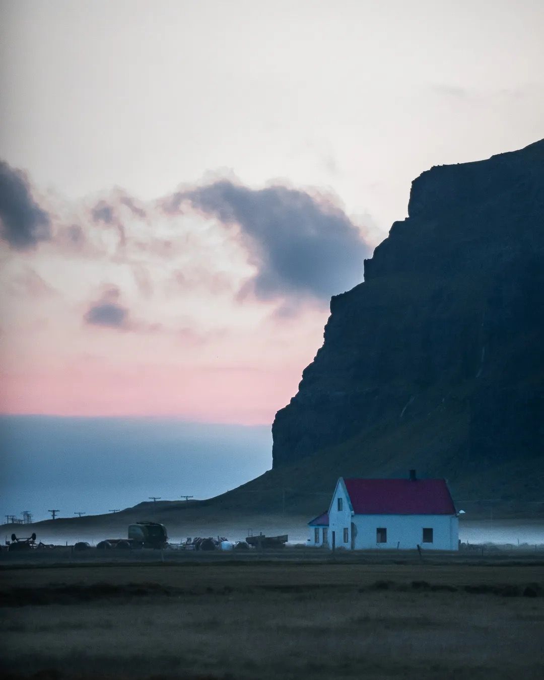 Small Icelandic house beneath a cliff at sunset with soft pink sky.