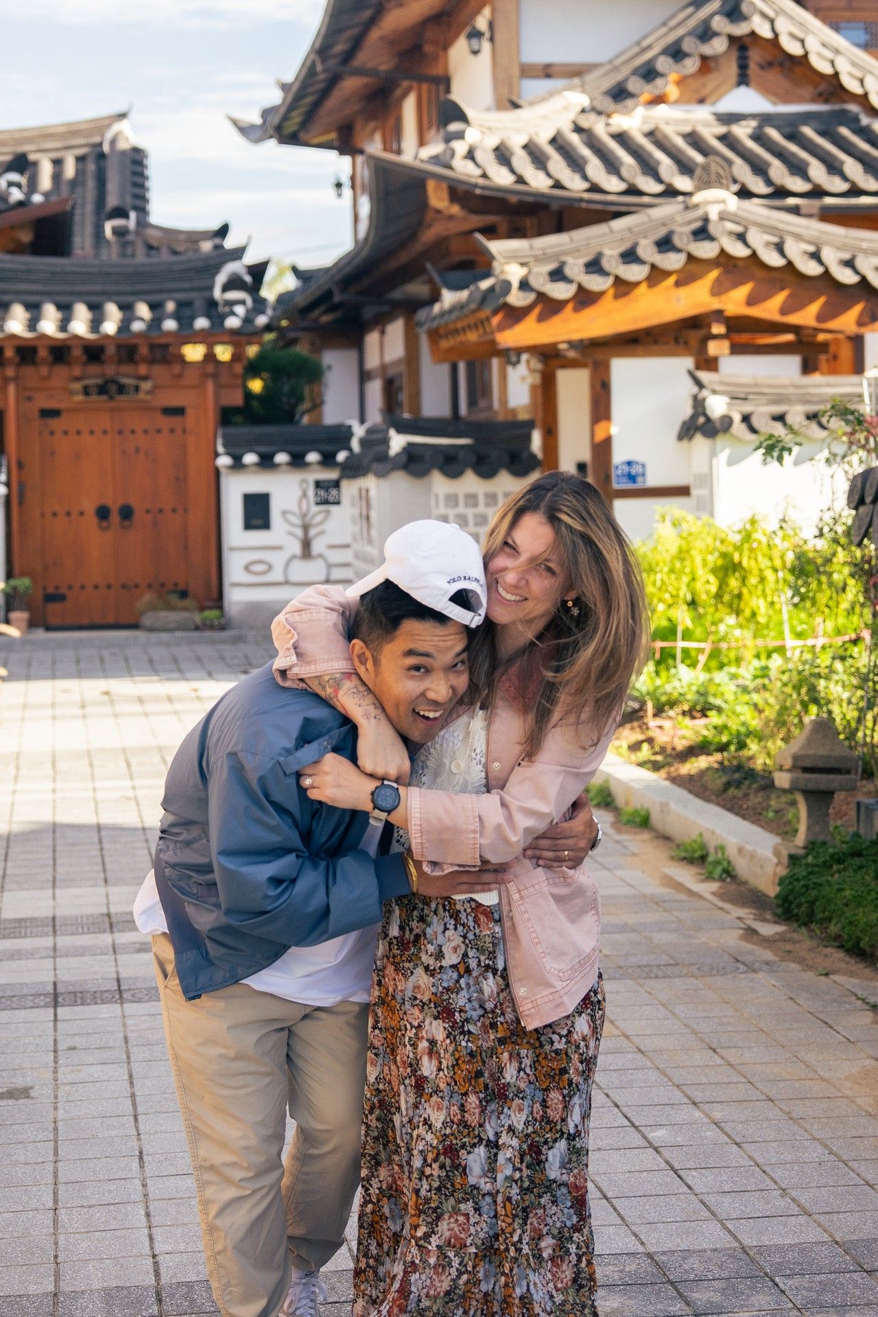 A couple shares joyful moments together at a traditional Korean hanok village with traditional architecture in the background.