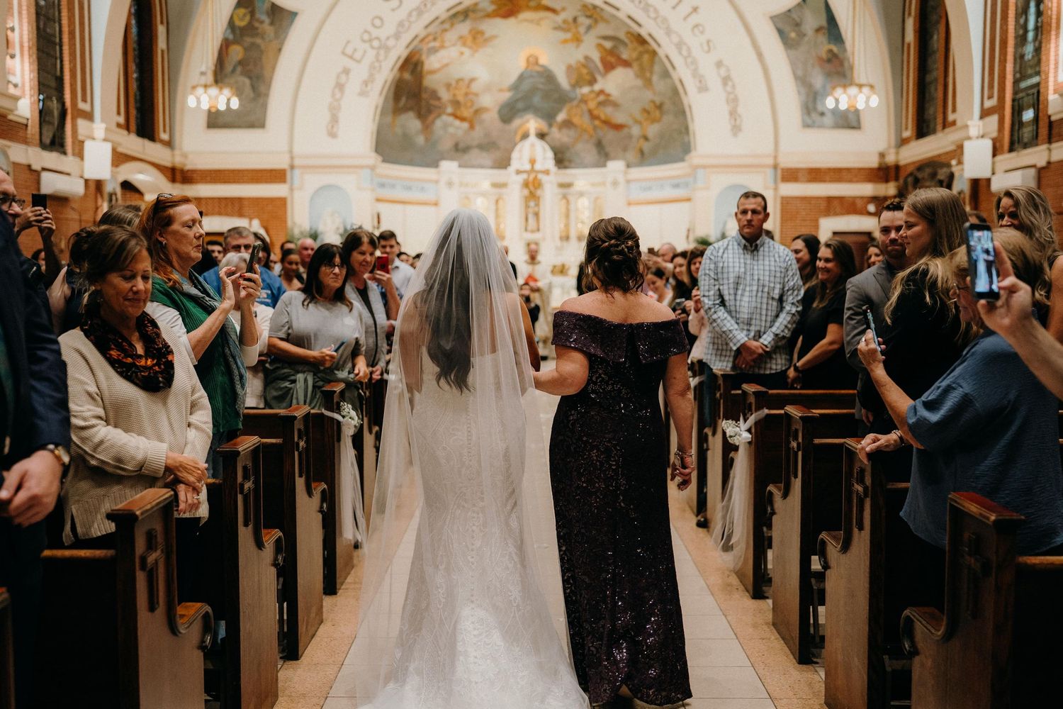 Wedding ceremony inside an ornate church with guests seated in wooden pews and a couple at the altar.