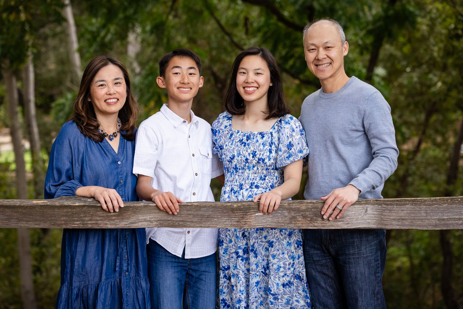 A family in coordinated blue and white outfits poses together on a wooden fence at Vasona Lake County Park in Los Gatos.