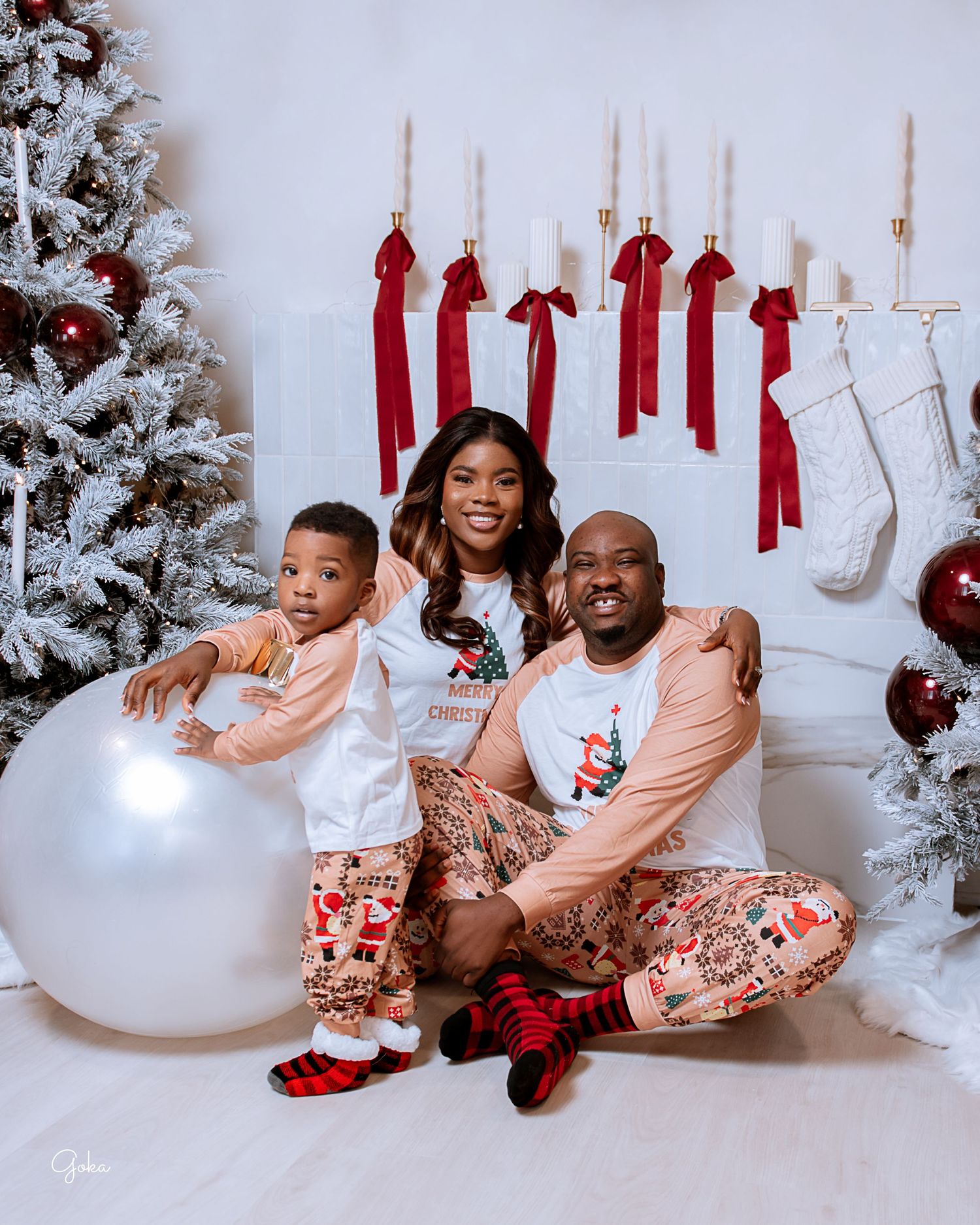 Family wearing matching floral pajamas sitting on white couch in holiday photoshoot.