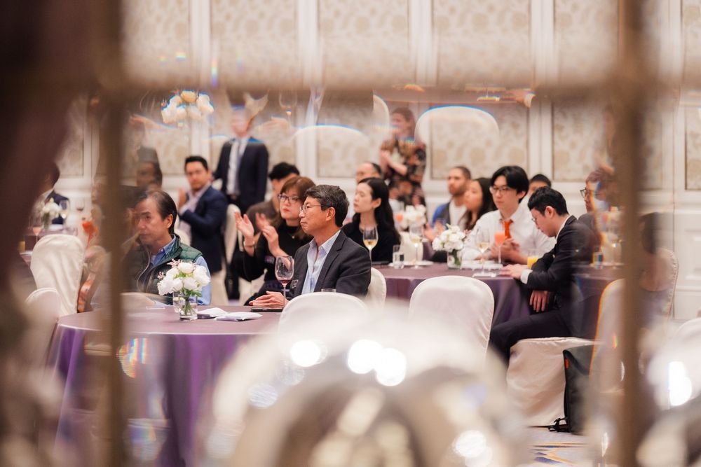 Wedding guests seated at elegant round tables with white linens and purple accents during a reception celebration.