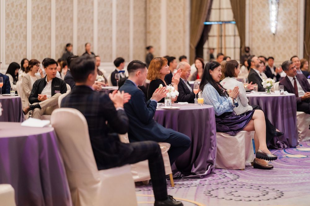 Business professionals seated in rows at a formal conference or meeting in an elegant hotel ballroom.