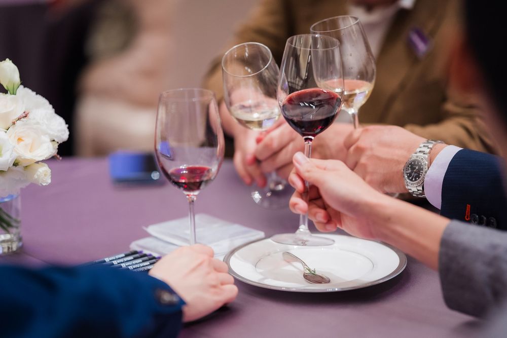 Multiple people enjoying red wine and food at a dining table with soft purple ambient lighting.