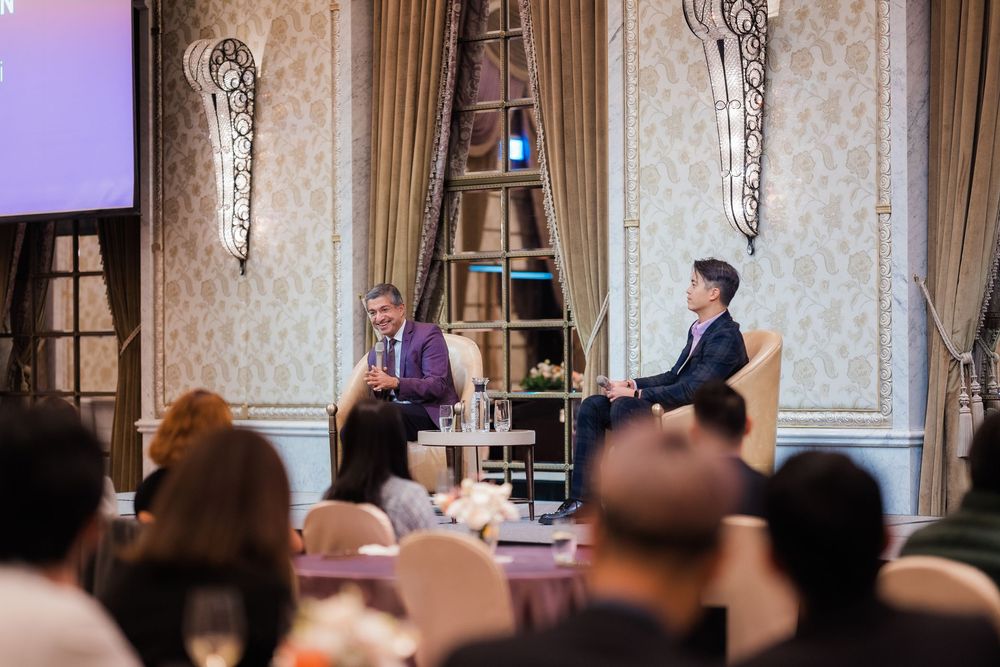 Business presentation in a formal meeting room with audience members seated at round tables.
