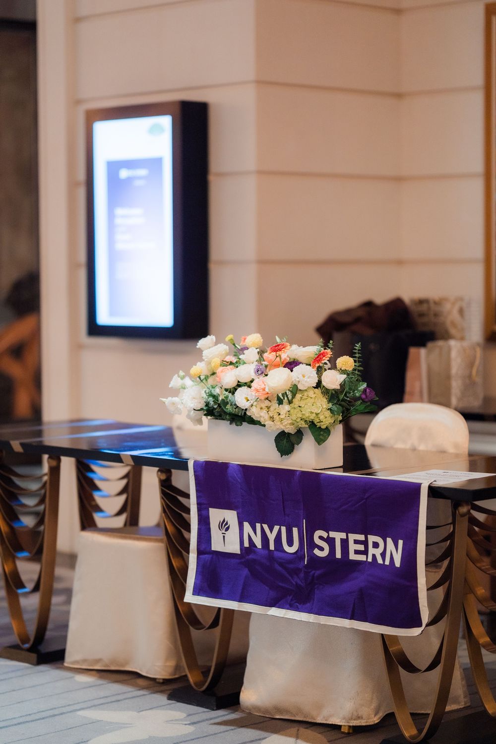 Purple NYU Stern branded banner displayed at an event with white floral centerpieces and covered chairs in the background.