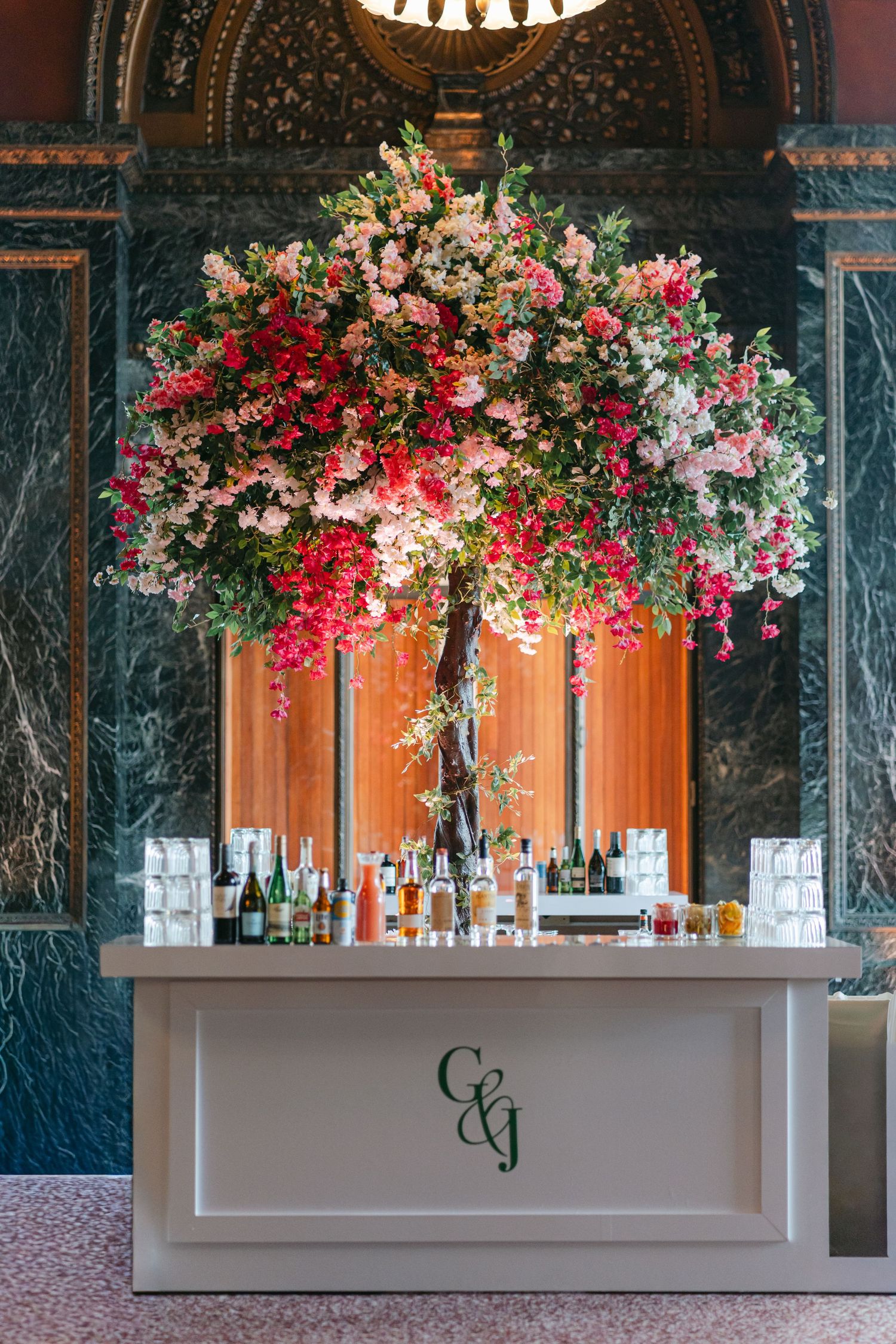 White wedding bar decorated with lush pink and red floral arrangements against an elegant marble wall backdrop.